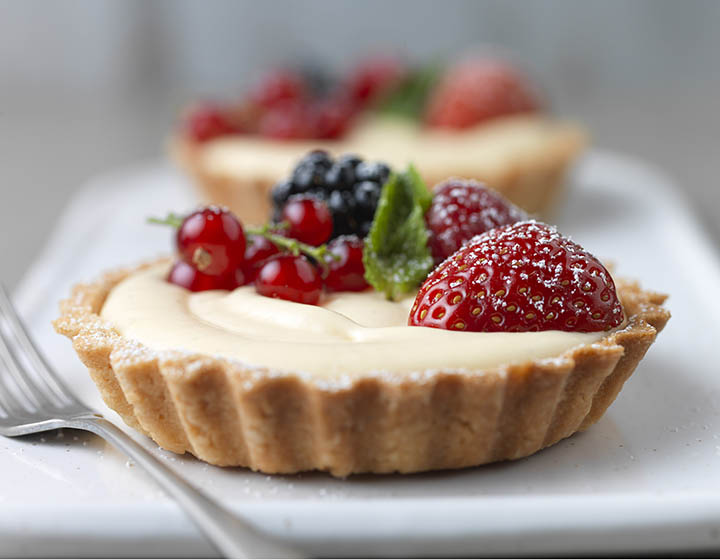 Cream and fruit filled pastry tart with raspberry, strawberry, blackberry and redcurrants, on plate with fork