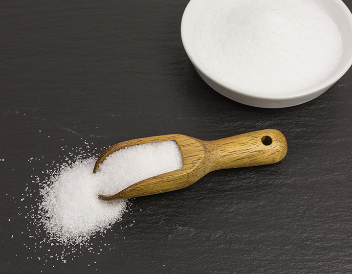 Wooden scoop of granulated sugar, next to white dish