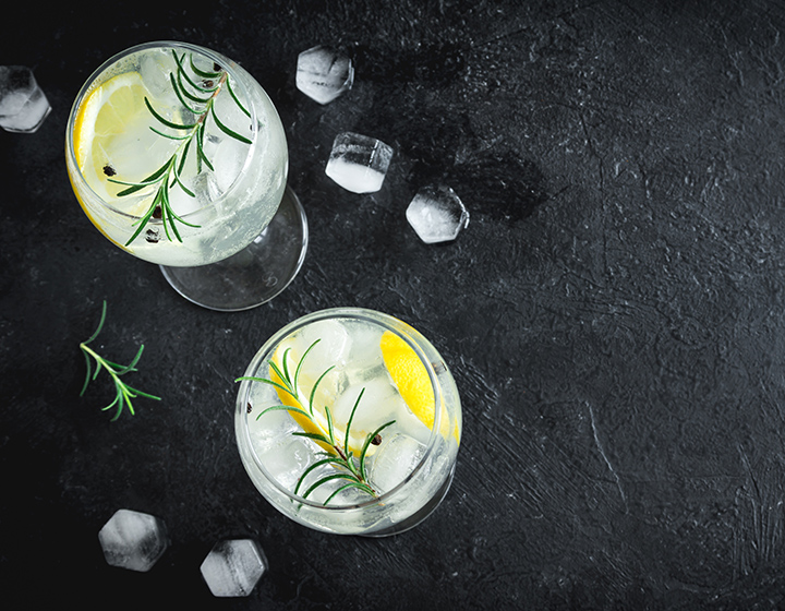 Two glasses of gin and tonic with ice, lemon and a sprig of rosemary
