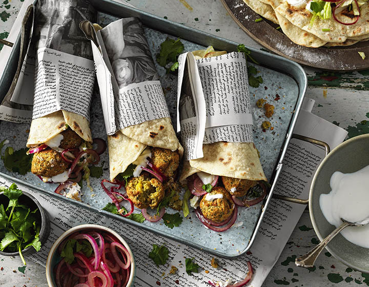 Three falafel flatbreads wrapped in newspaper on a metal tray