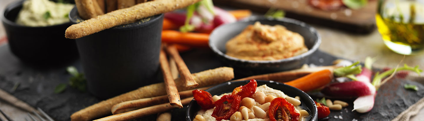 Antipasti plate with breadsticks, different flavours of hummus and fresh vegetables