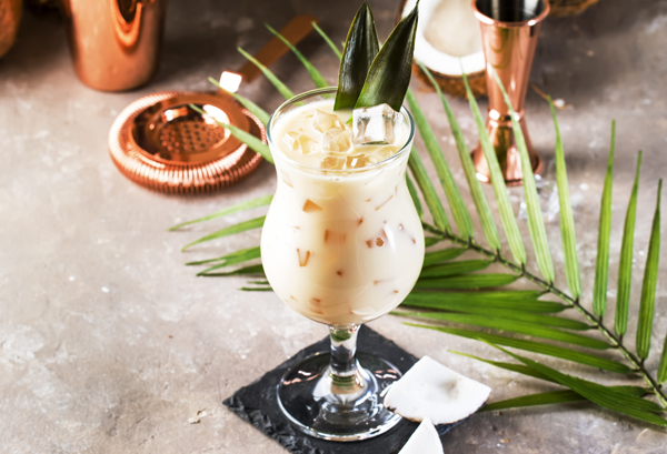 Pina Colada Cocktail on sand beige background with tropical fruits and bar tools, summer relaxation concept, copy space