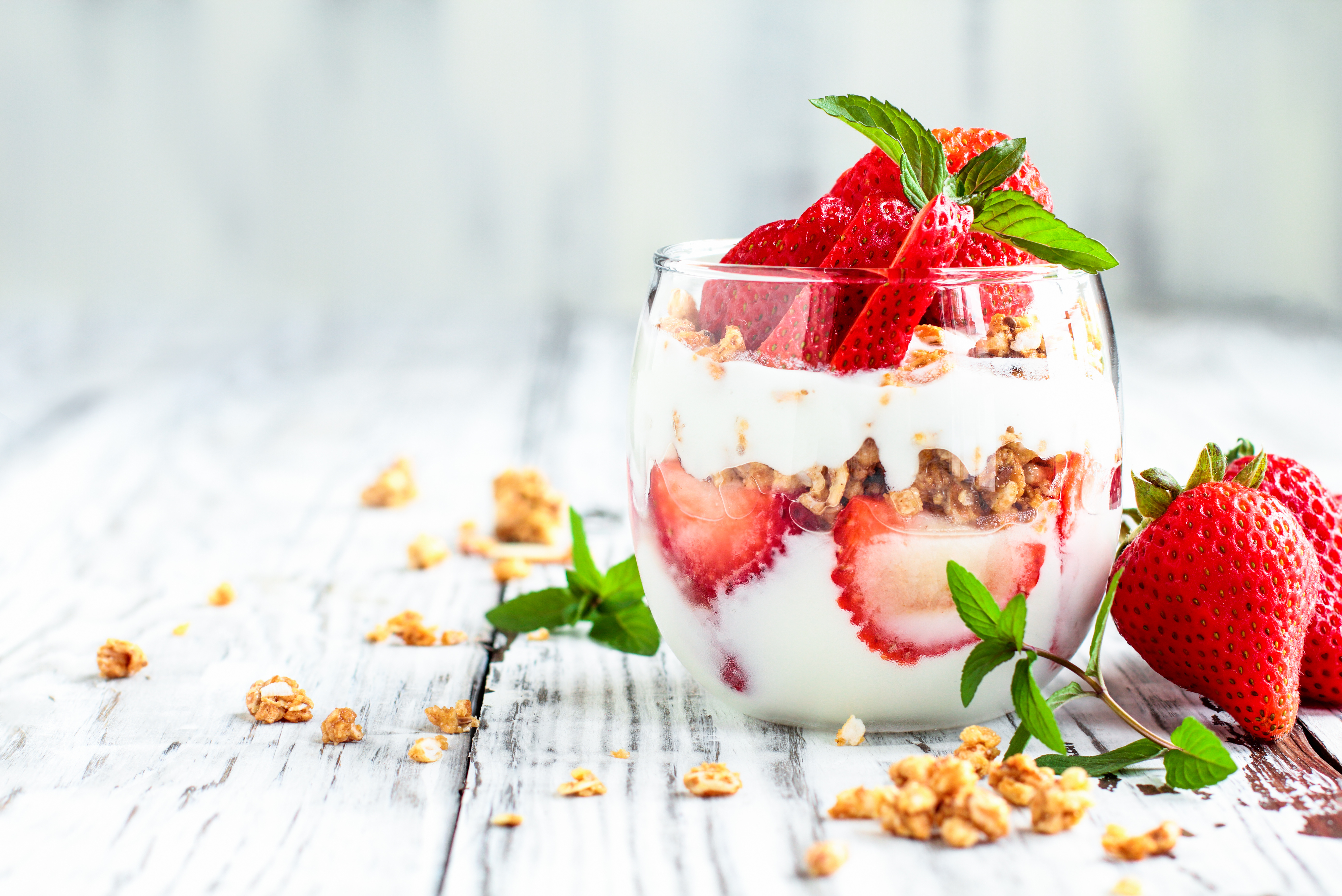 Healthy breakfast of strawberry parfaits made with fresh fruit, yogurt and granola over a rustic white table. Shallow depth of field with selective focus on glass jar in front. Blurred background and copy space.