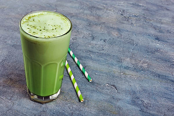 Organic green matcha tea latte in glass with cocktail straw on blue concrete background with copy space