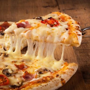 Slice of hot cheese pizza being lifted, showing melted stretchy mozzarella with toppings on a wooden table