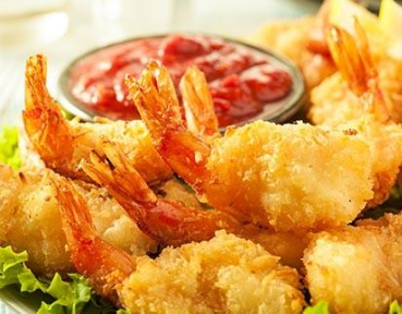 Crispy breaded shrimp served with a bowl of red dipping sauce on a bed of fresh greens