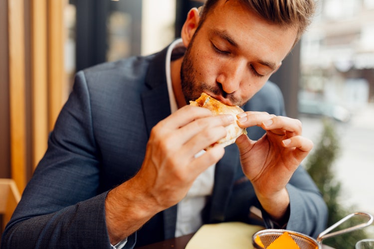Persona disfrutando una porción de pizza recién horneada, destacando la experiencia de consumo y la calidad de los ingredientes