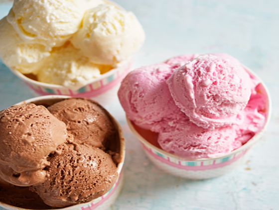 Three cups of ice cream in different flavors: vanilla, strawberry, and chocolate, served in pastel-striped containers on a light blue surface