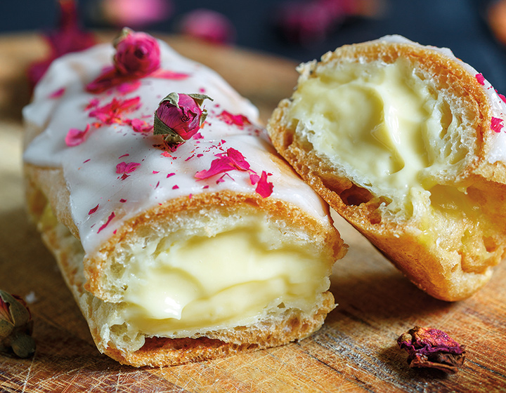 Cream filled eclair with white icing and pink rose garnish