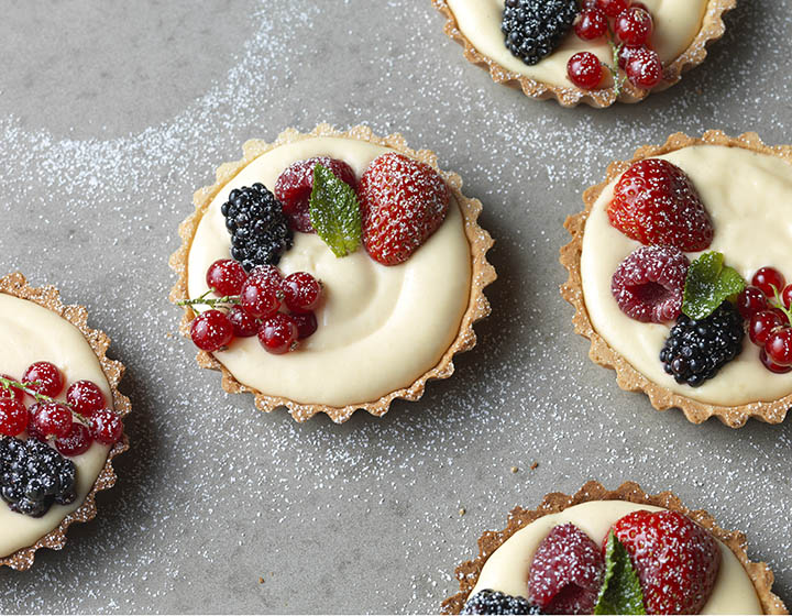 Cream and fruit filled pastry tarts with raspberries, strawberries, blackberries, redcurrants, and icing sugar