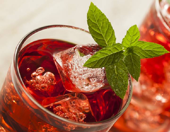 Red drink in a round glass with ice and a sprig of mint