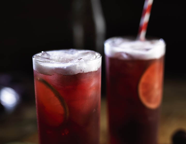 Two pink alcoholic drinks with ice, limes and striped straws