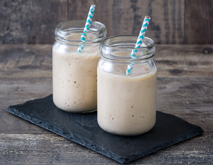 Two white protein shakes with striped straws in jars