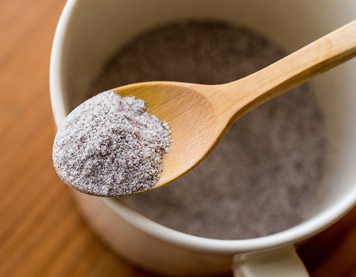 A spoon with hot chocolate powder above a mug of hot chocolate powder