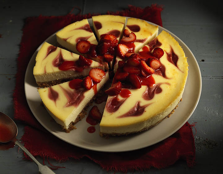 Yellow cheescake, topped with strawberries and cut into slices