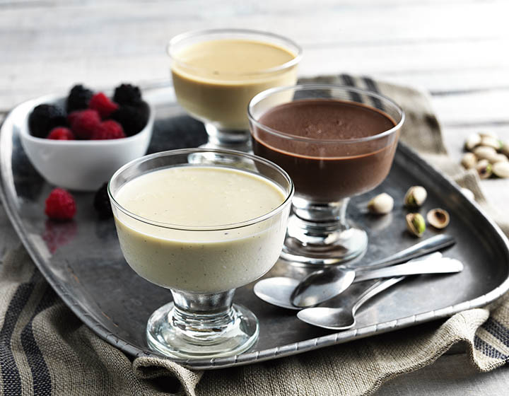 Three glasses of cream desserts with spoons and a bowl of berries