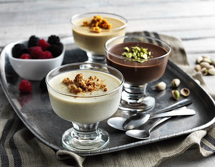 Glasses of cream desserts topped with pistachios and fruit