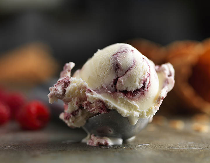 A single scoop of ice cream in an ice cream scoop with raspberries