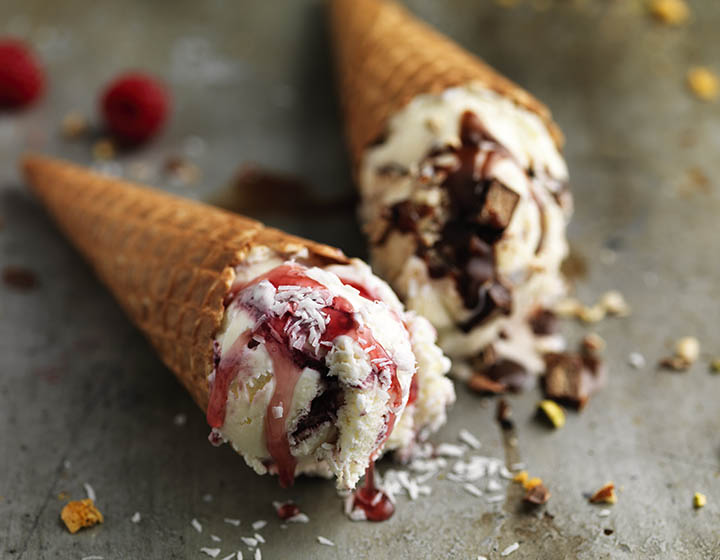 Two ice cream cones with white ice cream, one with pink sauce and one with brown