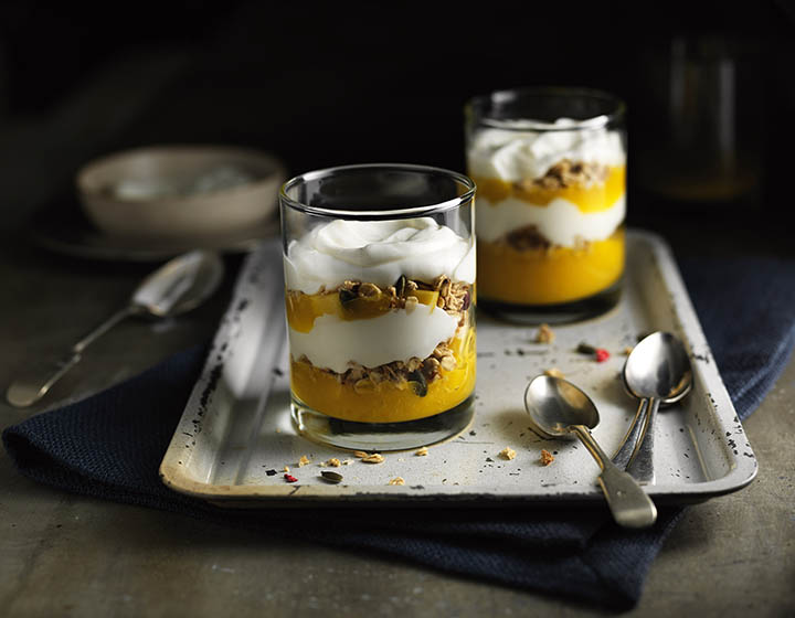 Two glasses of yoghurt with yellow fruit and granola