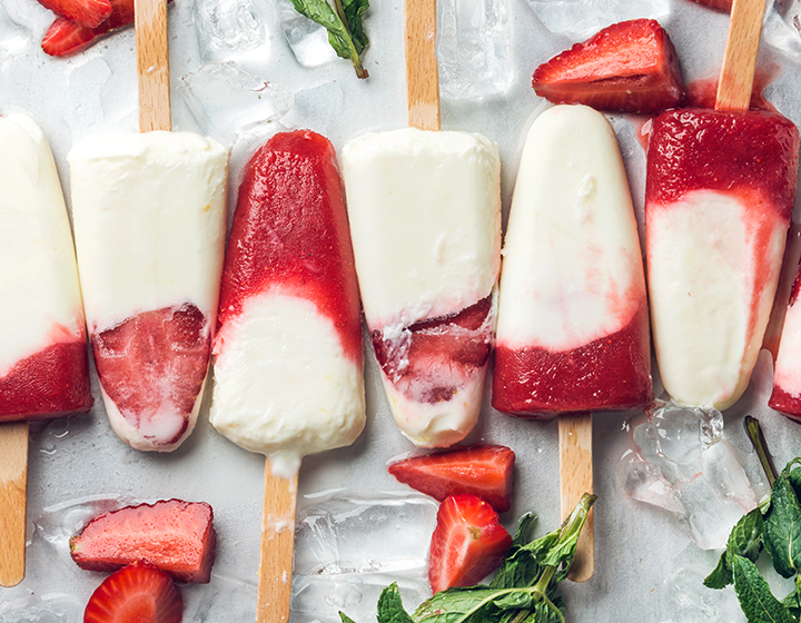 Red and white frozen yoghurt on sticks with cut strawberries