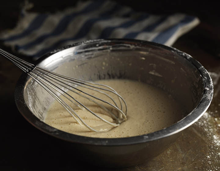 A whisk stirring a bowl of batter mix