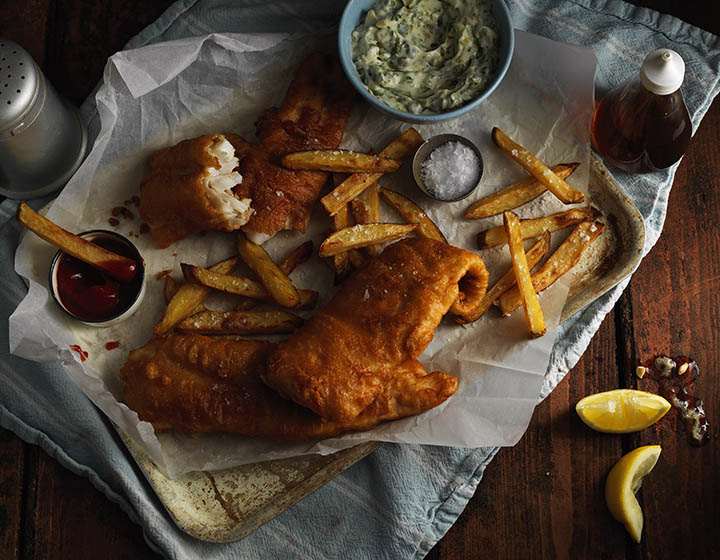 A tray of fish and chips with tartar sauce, ketchup and malt vinegar