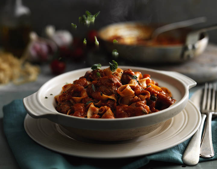 Sprinkling herbs on a bowl of pasta and tomato sauce