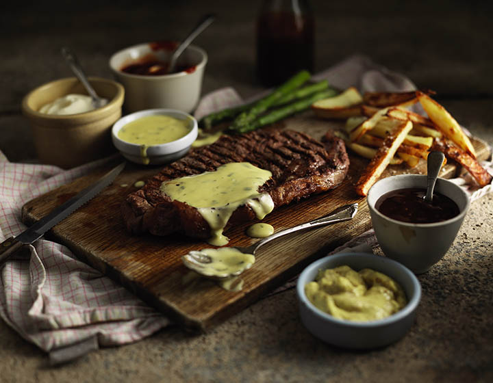 Steak, fries and asparagus on a chopping board with a green sauce
