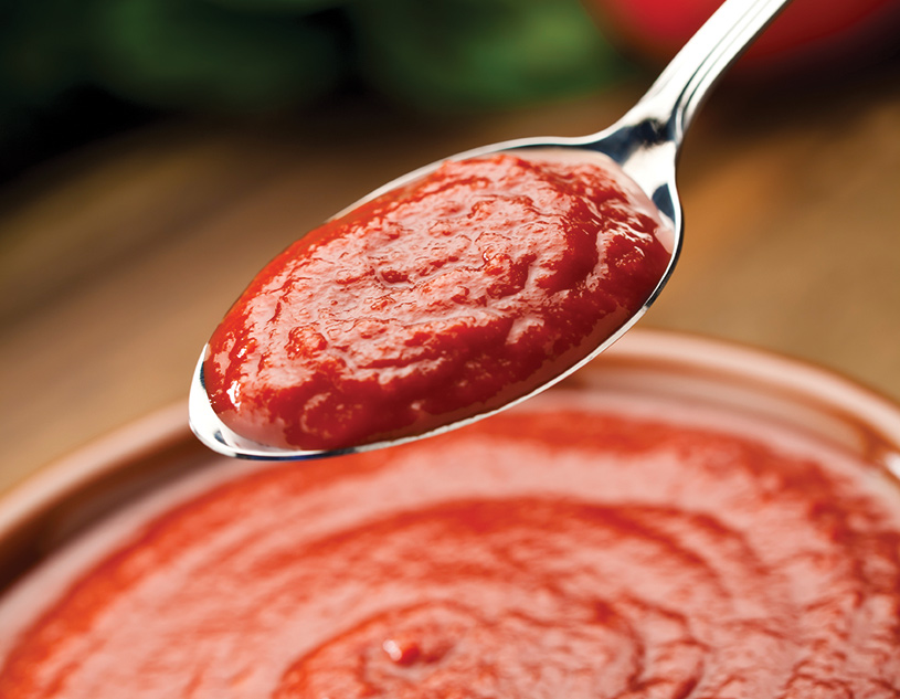 A spoonful of tomato sauce above a bowl 