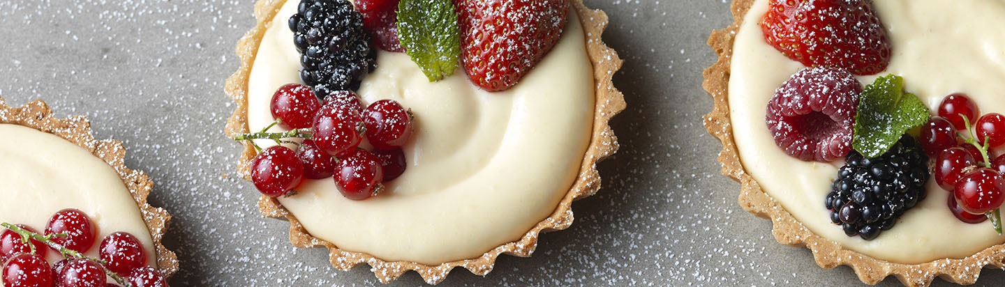 Three vanilla cream filled pastry tarts with fresh berries on top
