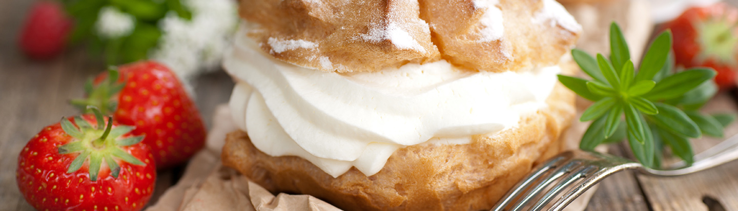 A choux pastry bun filled with fresh whipped cream, with a side of fresh strawberries