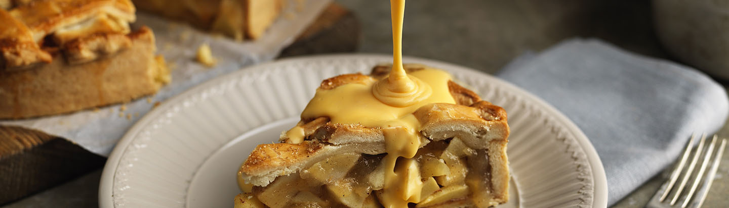 Pouring custard onto a slice of homemade apple pie on a plate