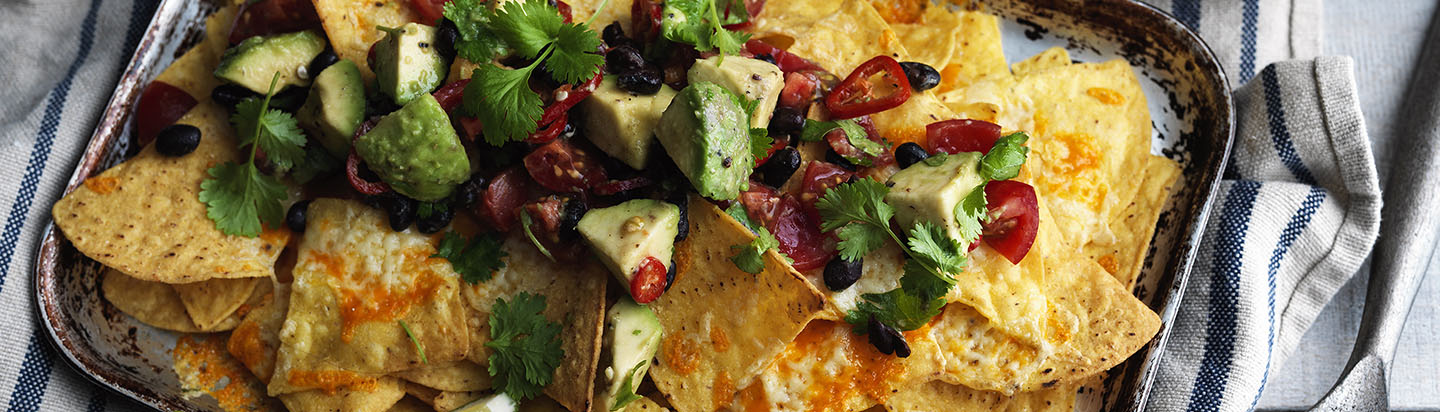 Baking sheet of cheesy tortilla chips with chopped chilies, herbs and avocado