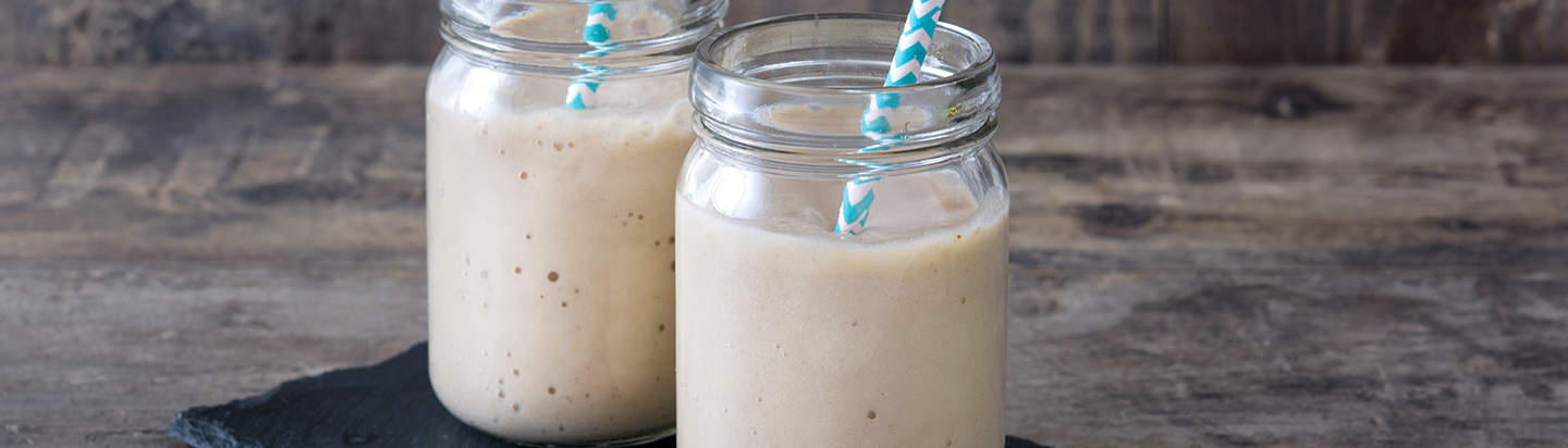 Two white protein shakes in jars with straws