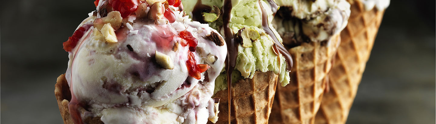 Four ice creams in cones with toppings and sauces