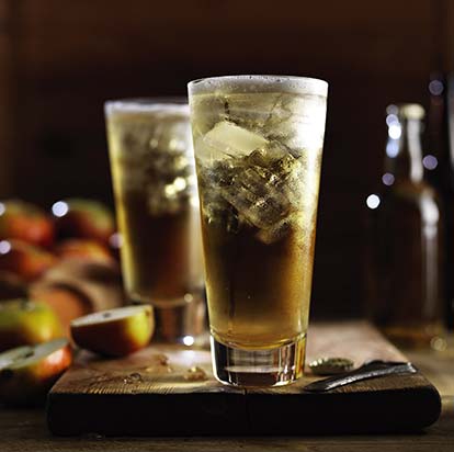 Sparkling cider in a glass with ice, sliced apple in the background