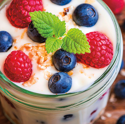 A jar of yoghurt topped with fresh raspberries, blueberries and a sprig of mint
