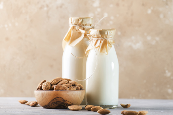 Vegan almond milk and cream in bottles, closeup, brown background. Non dairy alternative milk. Healthy vegetarian food and drink concept. Copy space