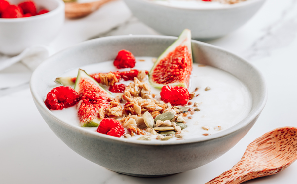 Granola with yogurt, figs and raspberries in bowls on white marble background. Selective focus