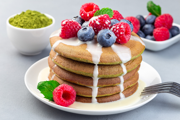 Matcha pancakes served with condensed milk, blueberry and raspberry on a white plate, horizontal, closeup