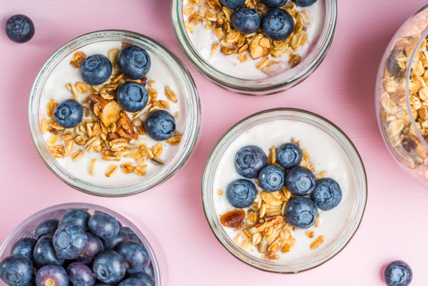 Breakfast from Fresh Natural Yogurt with Homemade Granola and Blueberries in Glass Jars on Light Pink Background