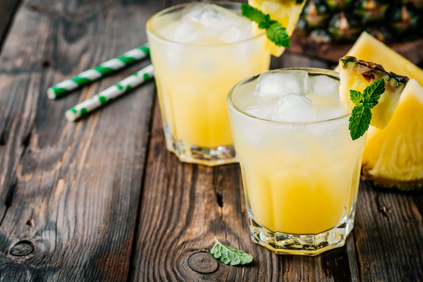 Fresh pineapple juice in two glasses with ice and mint leaves on dark rustic background