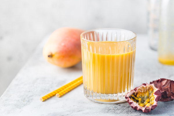 Tropical Mango smoothie in a glass and fresh mango on a light background. Mango shake. Tropical fruit concept.