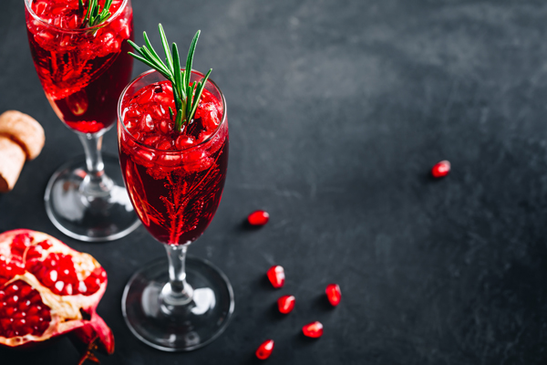 Pomegranate Champagne Cocktail with rosemary on gray concrete stone background, copy space