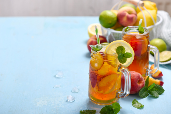 Iced tea with peaches, lemons, limes and mint with ice cubes, summer refreshment drink, cold fruit tea,  copy space background
