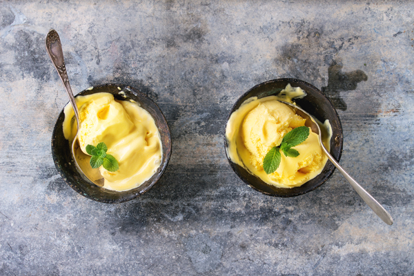 Homemade mango ice cream with fresh mint in vintage iron bowls over gray metal textured background. Flat lay