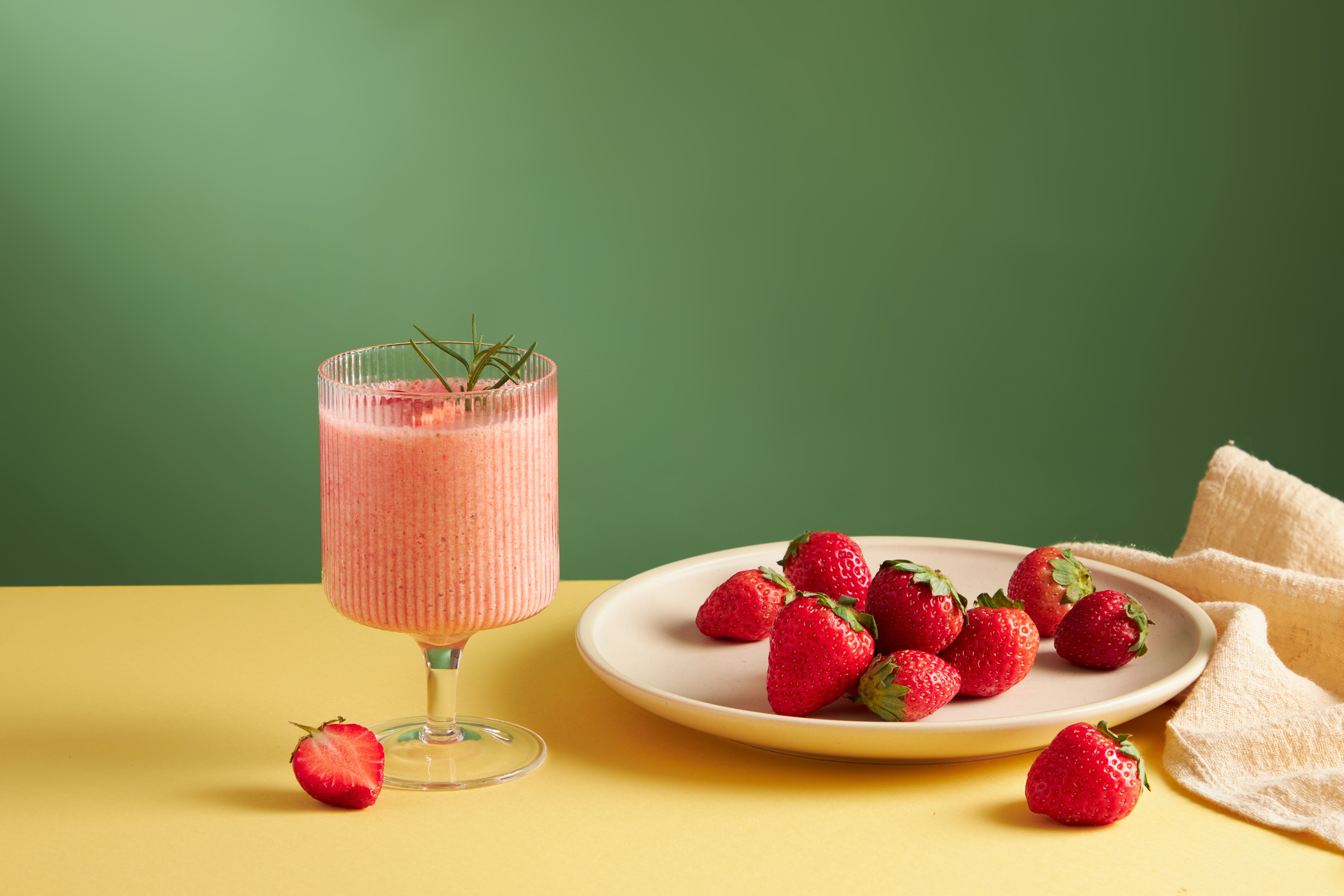 Strawberry smoothie in a cocktail glass with strawberry in a white dish decoration with green background for food advertising , front view
