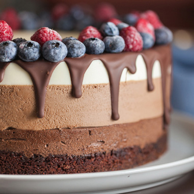 A three layer cake with chocolate drippings and berries showing texturizers in bakery applications