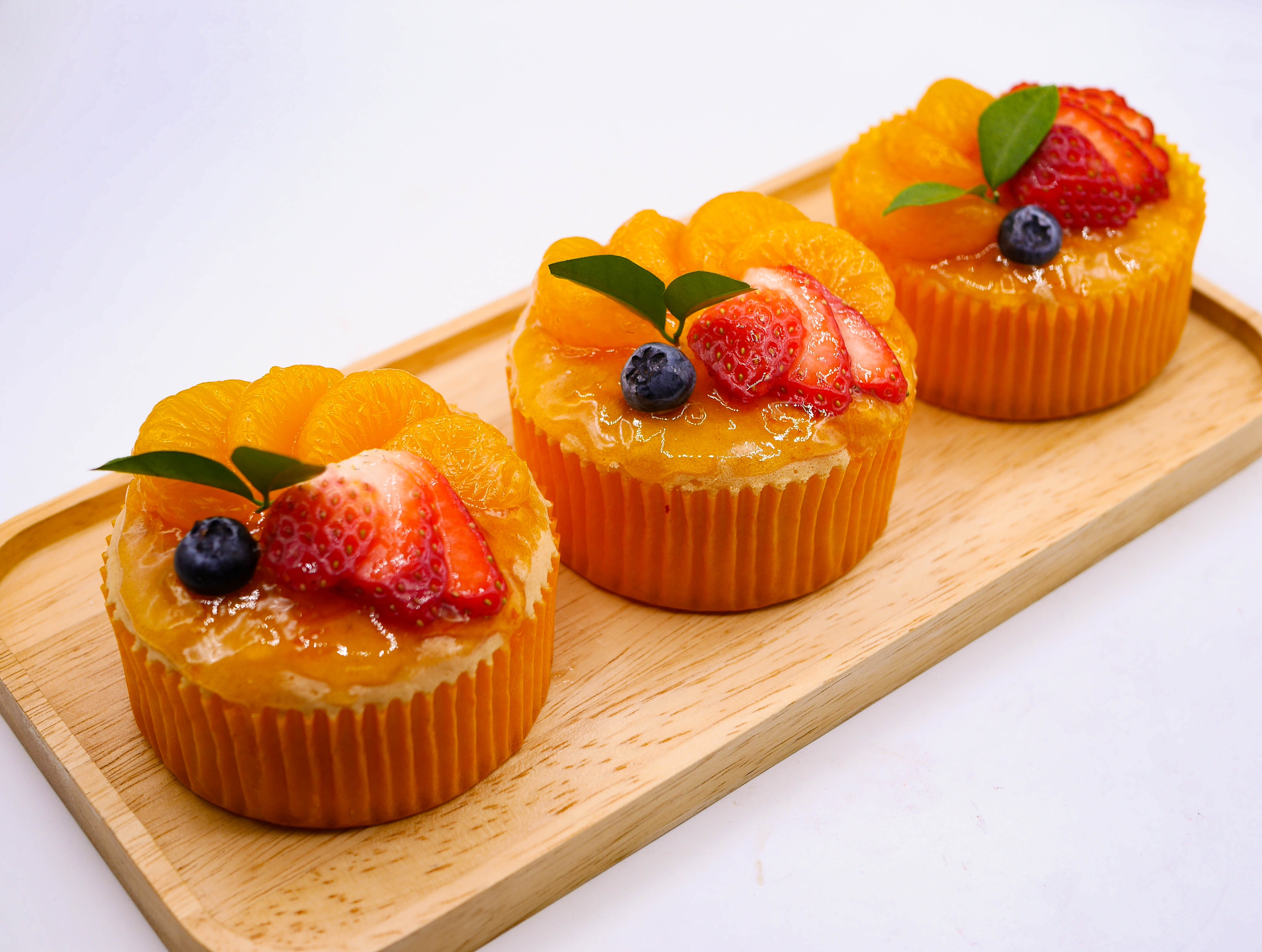 Fresh baked sweet and delicious mandarin orange sponge cake decorated with orange jelly sauce and orange pulp and Strawberry on  wood tray with white background. Homemade bakery concept for cafe